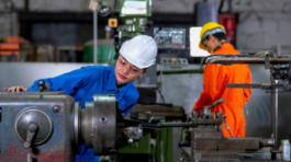 Asian factory worker woman look to part of the machine and inspect the function while her co-worker work with other machine in the background. Maintenance and check system support industrial business.