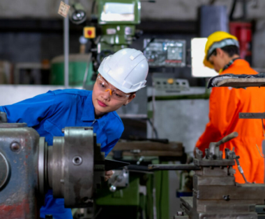 Asian factory worker woman look to part of the machine and inspect the function while her co-worker work with other machine in the background. Maintenance and check system support industrial business.